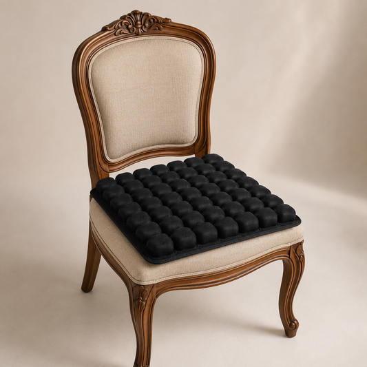 A classic wooden armchair with a beige upholstered seat and backrest, featuring a black textured bubble cushion on the seat, set against a neutral beige background.