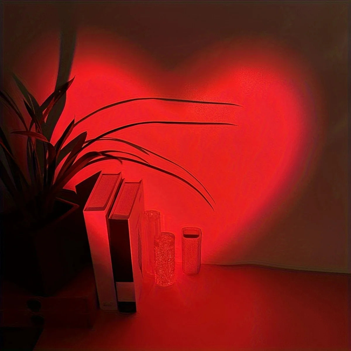 Red light casting a heart shape on a wall with books and a plant in the foreground.